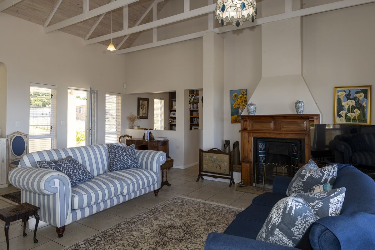 Spacious living room featuring a high vaulted ceiling with exposed trusses, tiled flooring, and a prominent wooden fireplace mantel.