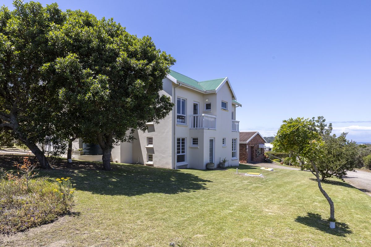 A view of the rear elevation of a two-story house featuring a green metal roof, balcony, and well-maintained garden area.