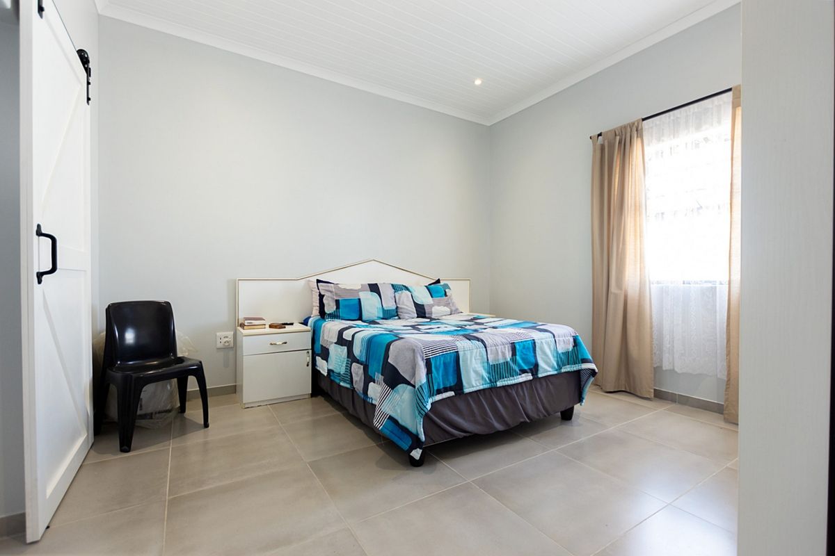 A well-maintained bedroom featuring neutral tiled flooring, a modern barn-style door, and recessed ceiling lighting, providing a clean and functional living space.