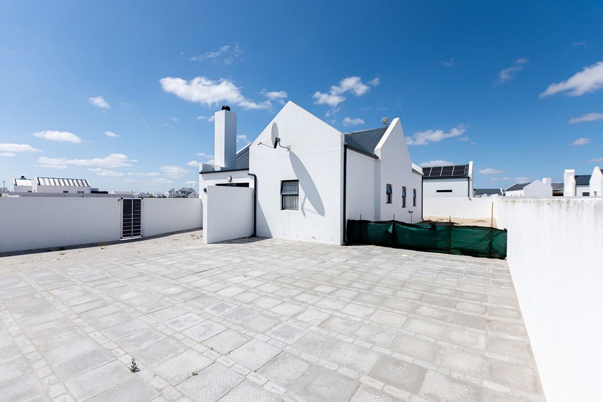 Rear view of the property featuring a paved courtyard area, white exterior walls, and a chimney stack.