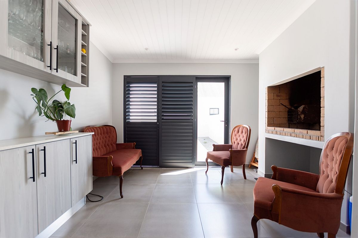 A bright living room featuring a brick fireplace, modern built-in cabinetry, tiled flooring, and shutter doors leading to an outdoor area.