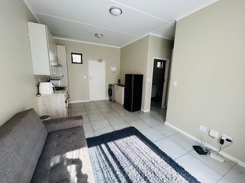 Open-plan living area featuring tiled flooring and a compact kitchen with built-in cabinetry and integrated sink.