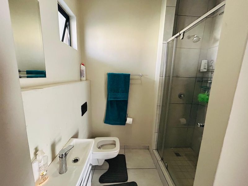 Compact bathroom featuring a glass-enclosed shower, wall-mounted toilet, and a modern vanity basin with neutral tiling throughout.