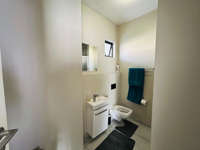 A compact bathroom featuring a wall-mounted vanity with basin, wall-mounted toilet, and tiled flooring, with some visible ceiling staining.