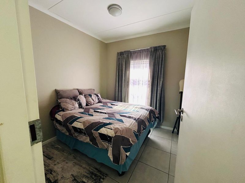 A functional bedroom featuring tiled flooring, neutral wall tones, and a window with installed curtain tracks.