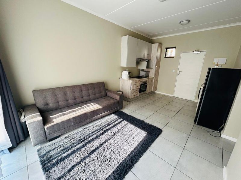 Open-plan living area featuring a compact kitchen with built-in cabinetry, oven, and hob, complemented by neutral tiled flooring throughout.