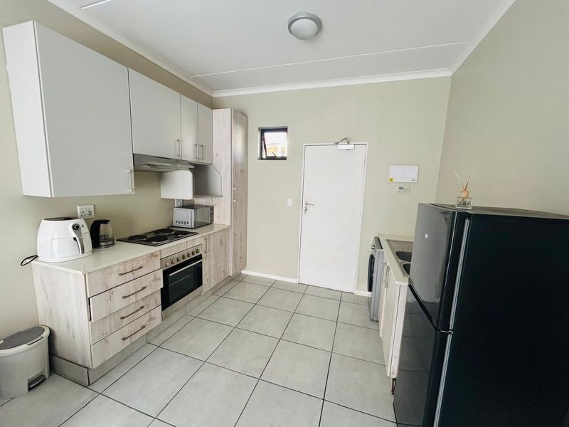 A functional kitchen featuring light wood-grain cabinetry, built-in oven and hob, tiled flooring, and a dedicated sink area with direct exterior access.