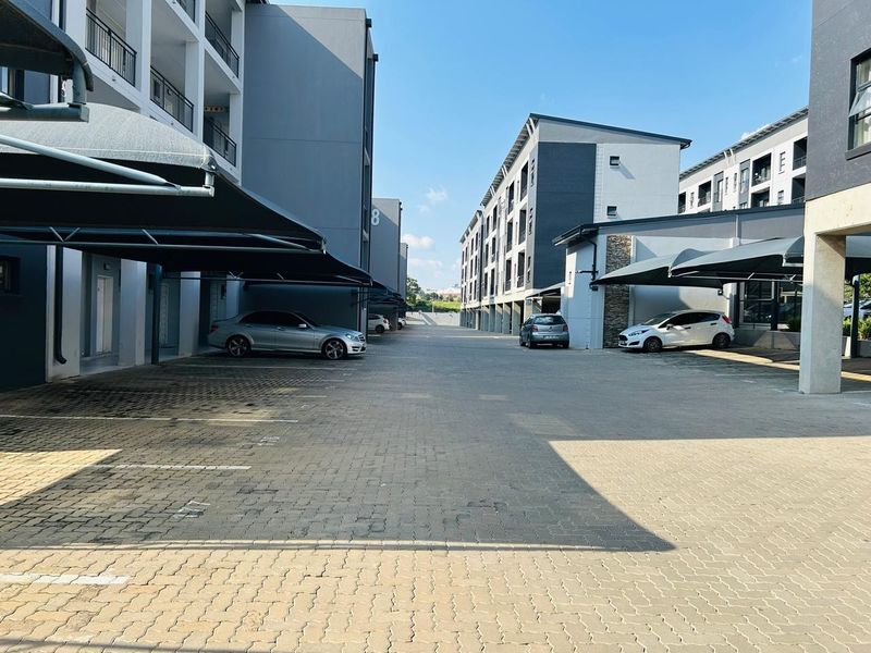 Exterior view of a modern apartment complex featuring paved parking areas with covered bays and multi-story residential buildings.
