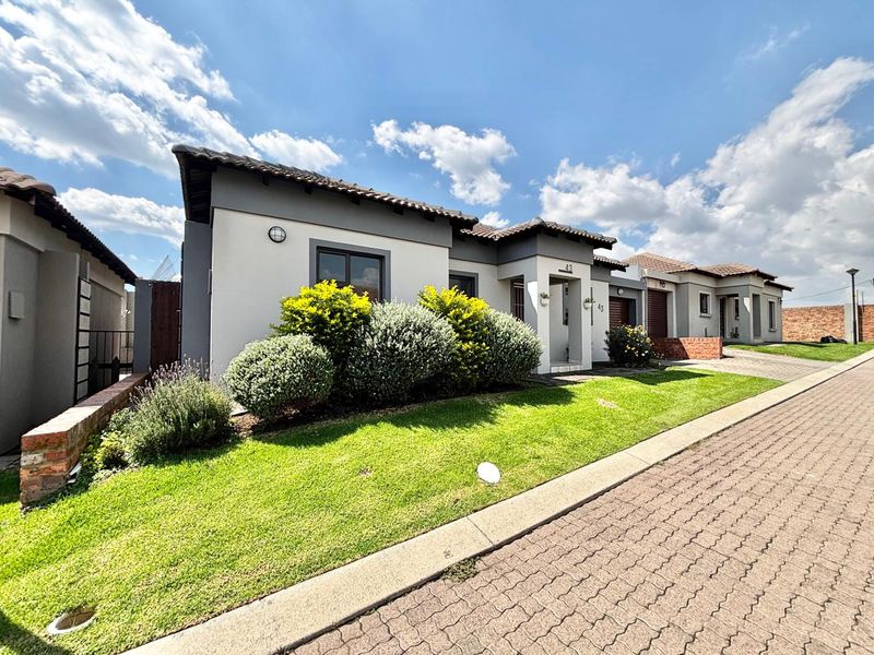 Front elevation of a modern townhouse featuring a tiled roof, paved driveway, and well-maintained garden area.