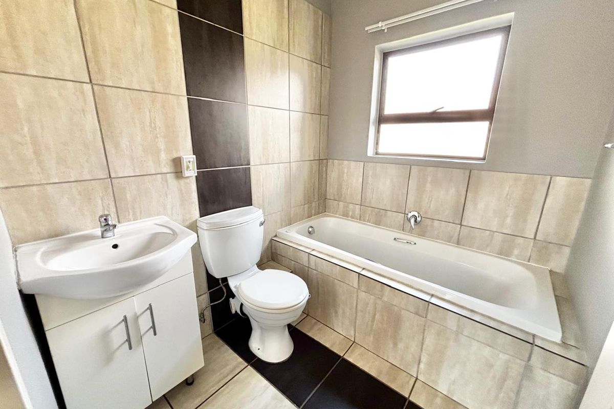 A clean, functional bathroom featuring a built-in bathtub, vanity cabinet with basin, and neutral-toned wall and floor tiling.