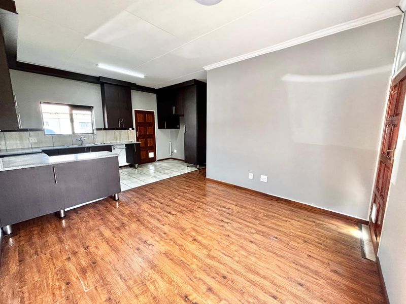 Open-plan living area featuring laminate flooring, a modern kitchen with dark cabinetry, stone countertops, and a tiled kitchen floor.