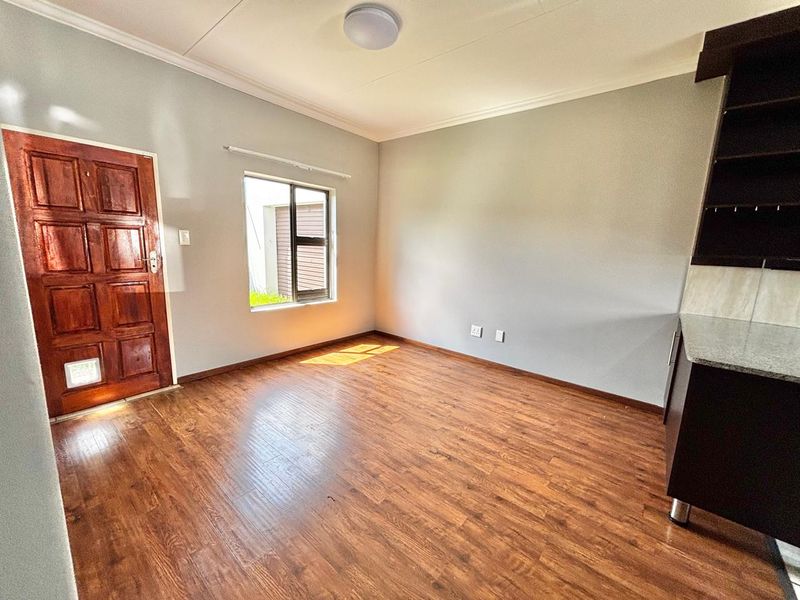 An open-plan living area featuring laminate flooring, a timber entrance door with a pet flap, and a section of built-in kitchen cabinetry.