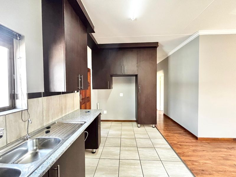 A clean, empty kitchen featuring dark wood cabinetry, granite countertops, a stainless steel sink, and a combination of tiled and laminate flooring.
