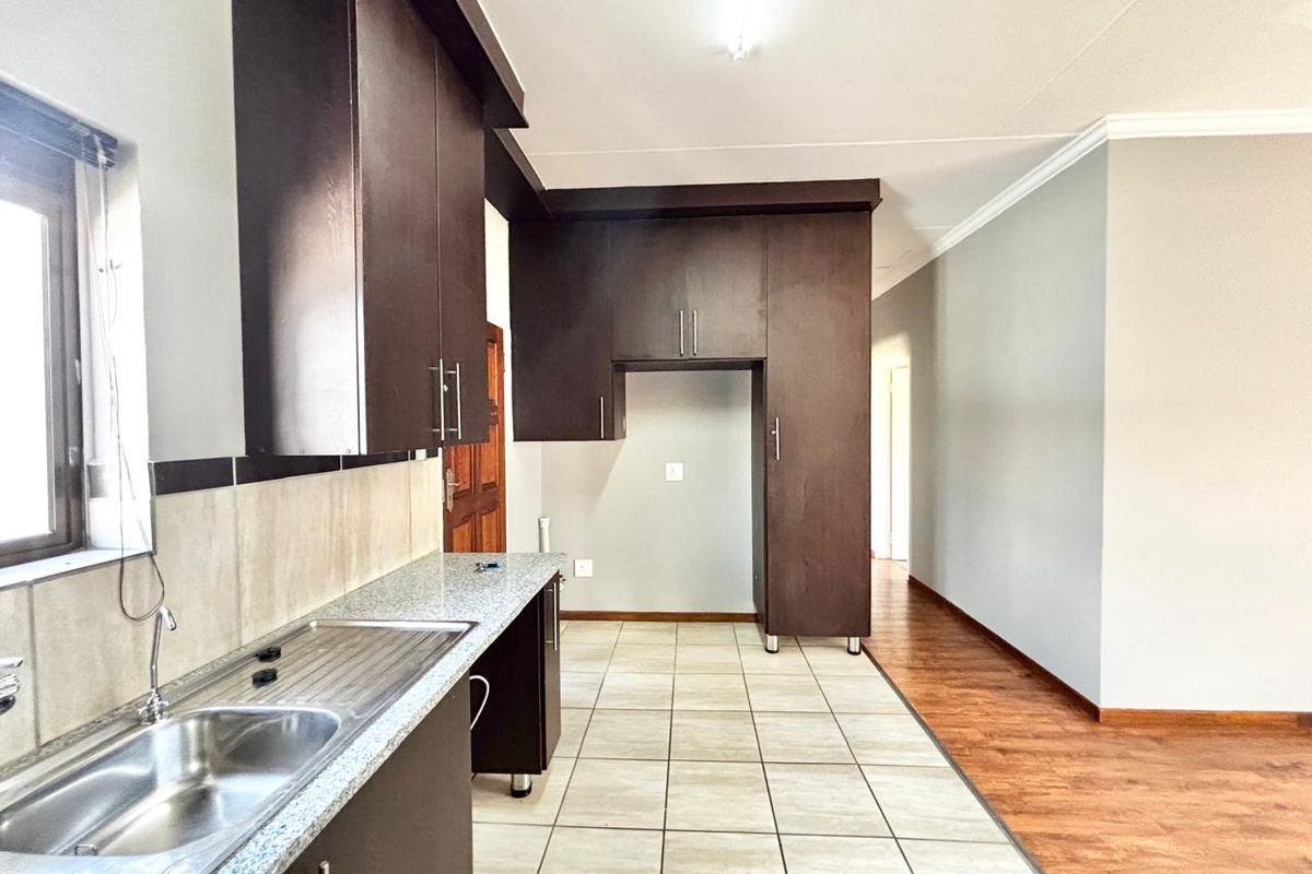 A clean, empty kitchen featuring dark wood cabinetry, granite countertops, a stainless steel sink, and a combination of tiled and laminate flooring.