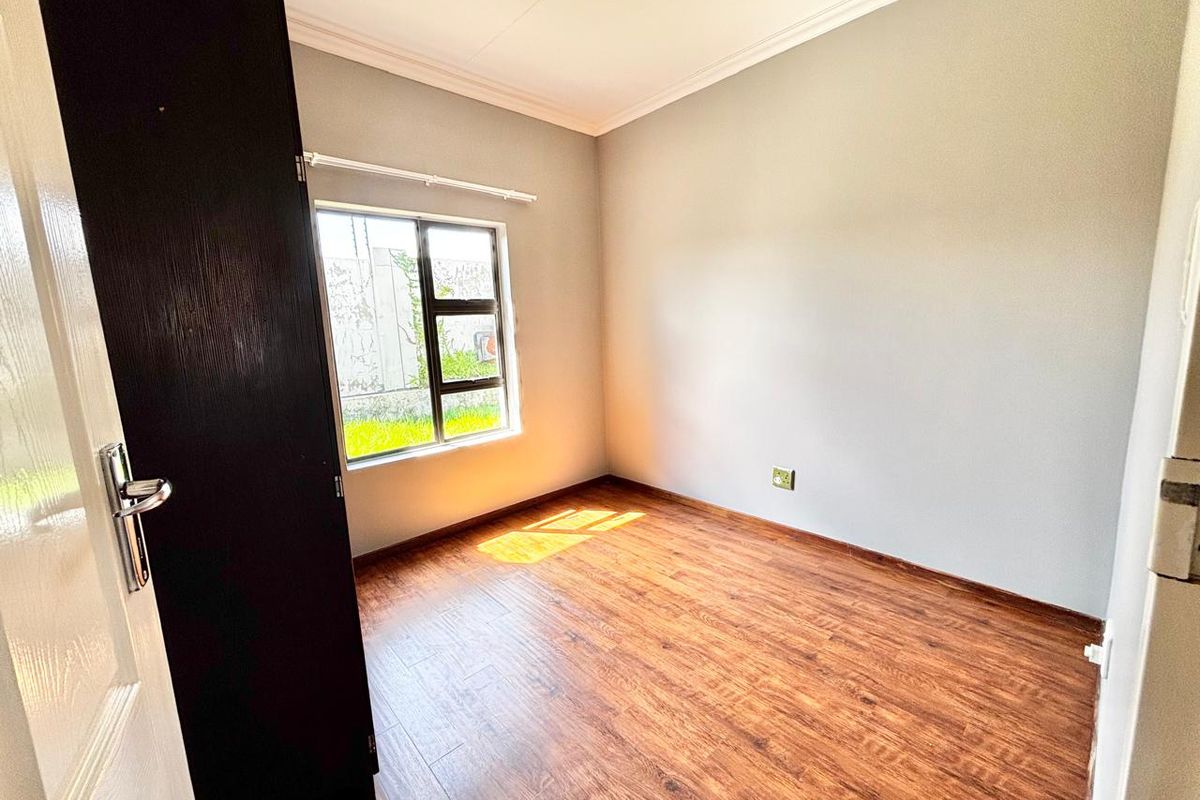 A bright, empty bedroom featuring modern laminate flooring, a built-in cupboard, and neutral wall finishes, ready for personalization.