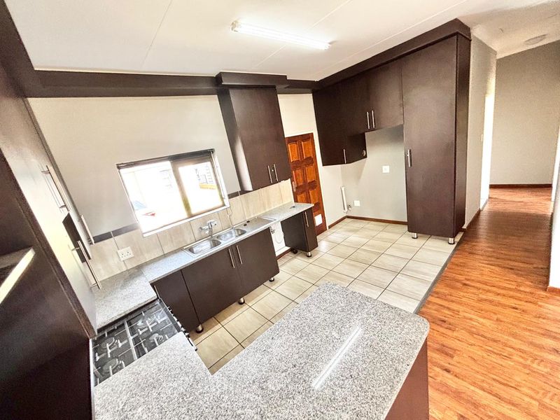 A functional kitchen featuring dark cabinetry, granite countertops, a double basin sink, and a gas hob, with a mix of tiled and laminate flooring.