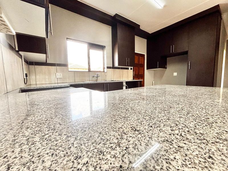 Modern kitchen featuring extensive granite countertops, ample built-in cabinetry, and a tiled backsplash, offering a clean and functional workspace.