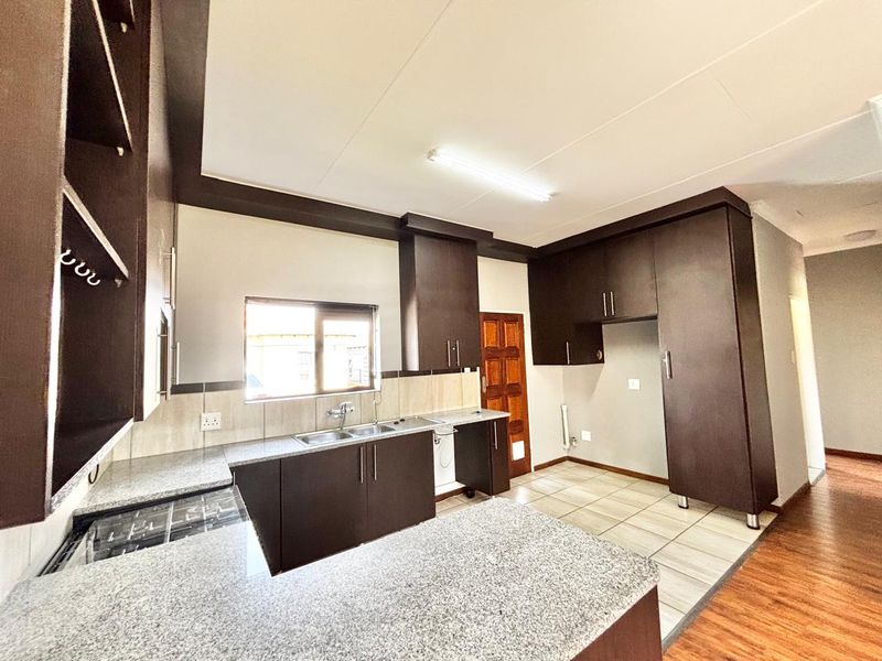 A clean, functional kitchen featuring dark cabinetry, granite countertops, a double basin sink, and a built-in gas hob with tiled and laminate flooring.