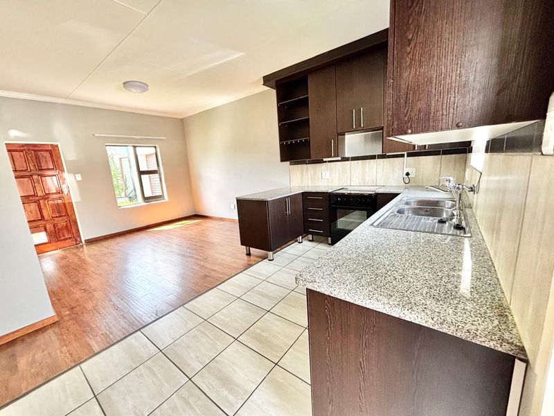 Open-plan living area featuring a modern kitchen with granite countertops, built-in oven, and a seamless transition between tiled kitchen and laminate living room flooring.