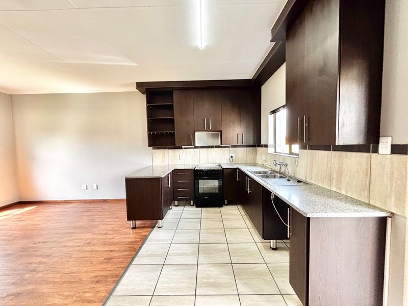 Open-plan kitchen featuring dark wood cabinetry, granite countertops, and a freestanding stove, seamlessly transitioning into a spacious living area with laminate flooring.