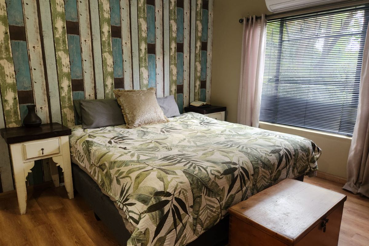A cozy bedroom featuring laminate flooring, a wall-mounted split-system air conditioner, and a decorative feature wall with venetian blinds.