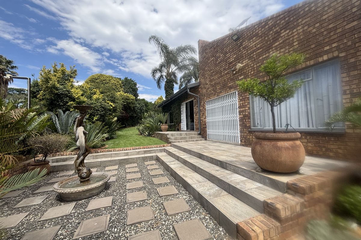 A well-maintained rear garden featuring a tiled patio, face brick exterior, and a decorative water feature set within a landscaped outdoor space.