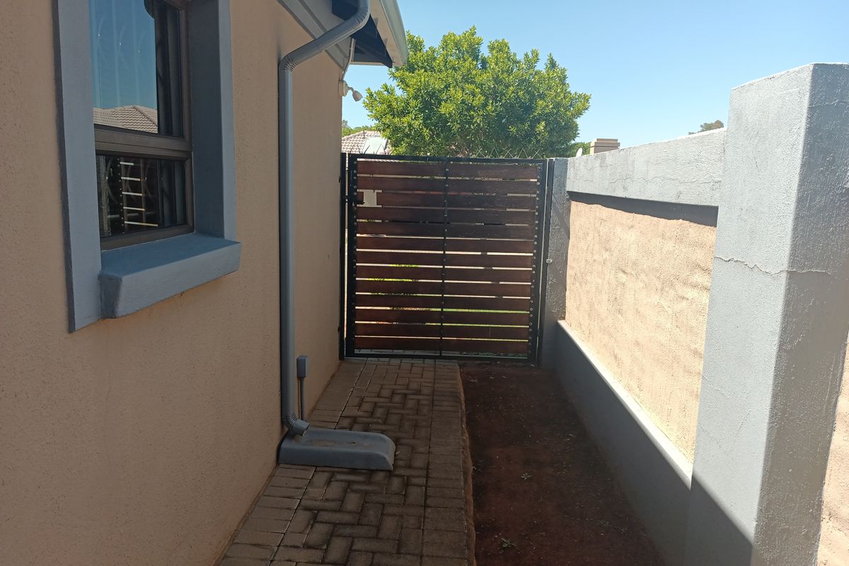 A side passage featuring a paved walkway, timber slat gate, and boundary wall with visible plaster cracking.
