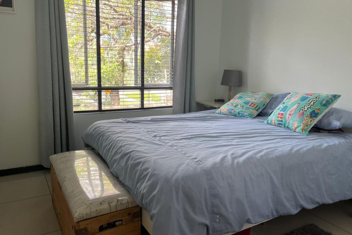 A bright bedroom featuring large windows with natural light and neutral tiled flooring, offering a comfortable and functional living space.