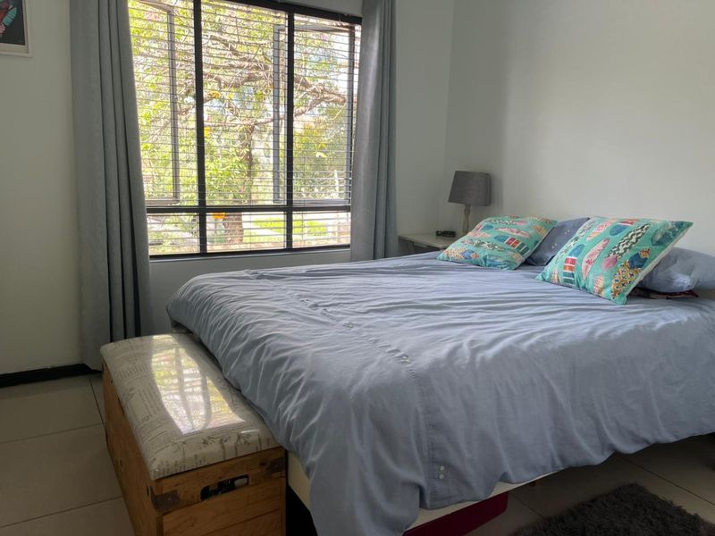 A bright bedroom featuring large windows with natural light and neutral tiled flooring, offering a comfortable and functional living space.