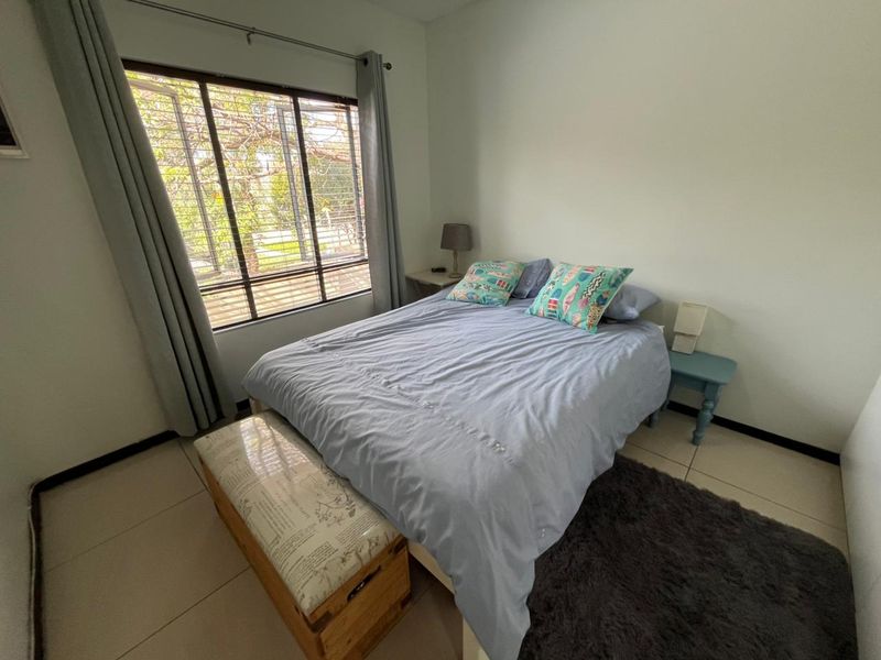 A functional bedroom featuring tiled flooring and a large window with security bars, providing natural light and a view of the exterior.