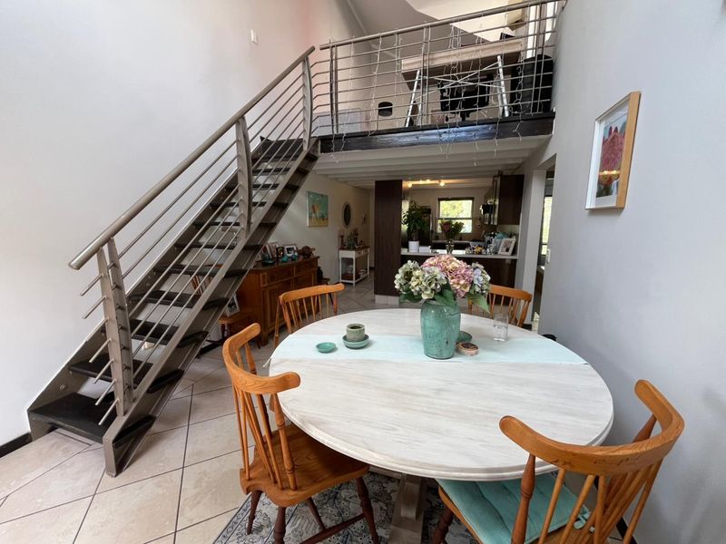 Open plan dining area featuring a modern metal staircase leading to a mezzanine level with tiled flooring throughout.