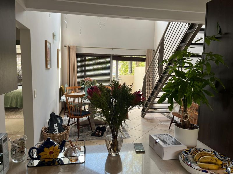 Open-plan living and dining area featuring a modern staircase with metal balustrade, tiled flooring, and access to an outdoor patio through sliding glass doors.