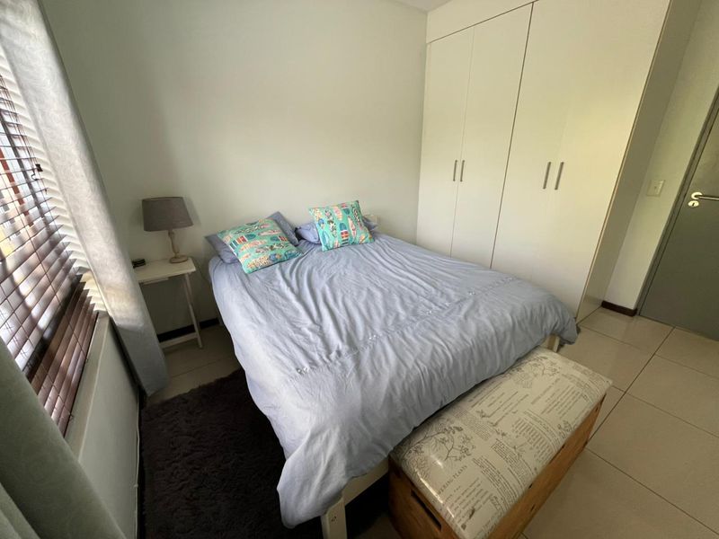 A functional bedroom featuring built-in cupboards, tiled flooring, and venetian blinds, offering a clean and practical living space.