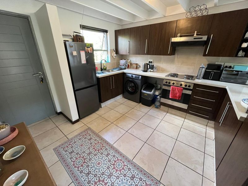 A functional kitchen featuring dark wood cabinetry, light countertops, tiled flooring, and integrated appliances including an oven, hob, and extractor fan.