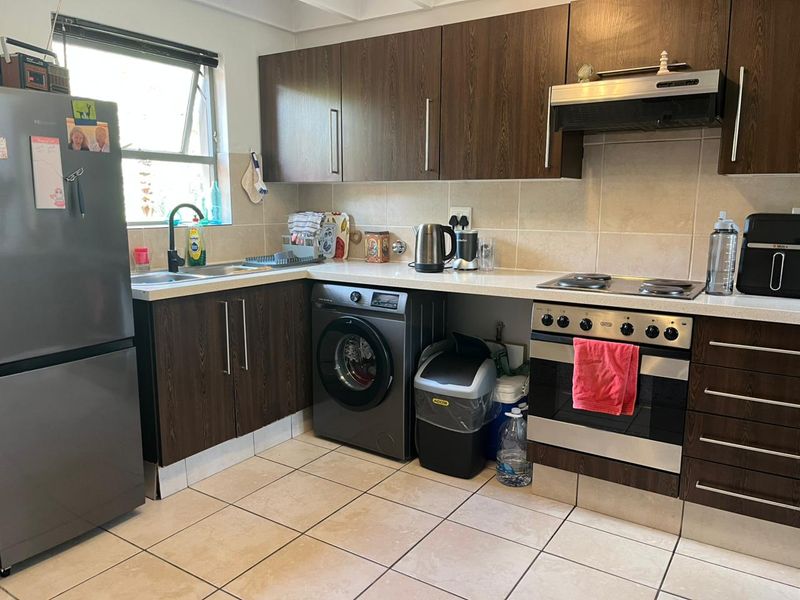A functional kitchen featuring dark wood cabinetry, stone countertops, integrated oven with hob, extractor fan, and tiled flooring with a neutral backsplash.