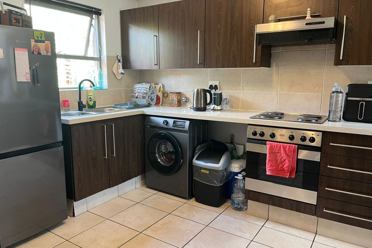 A functional kitchen featuring dark wood cabinetry, stone countertops, integrated oven with hob, extractor fan, and tiled flooring with a neutral backsplash.