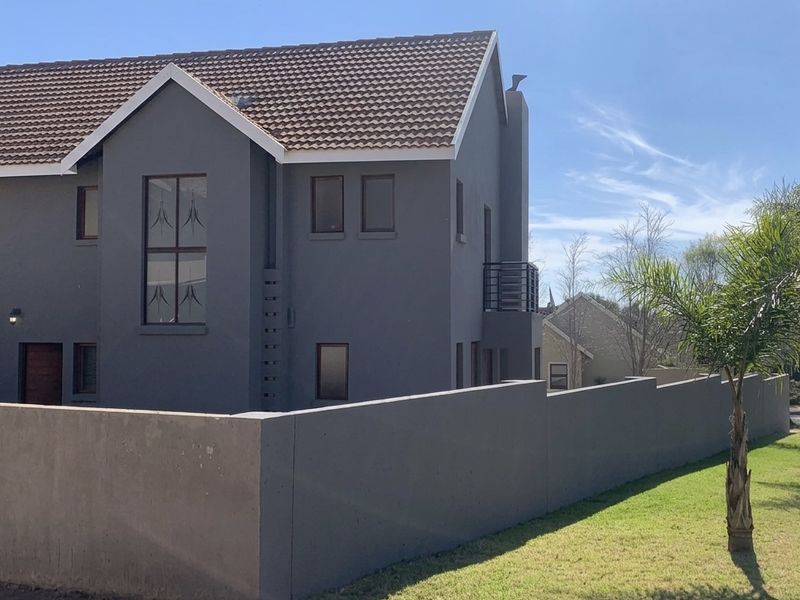 A modern double-story house featuring a grey exterior finish, tiled roof, and a secure boundary wall with a small balcony.