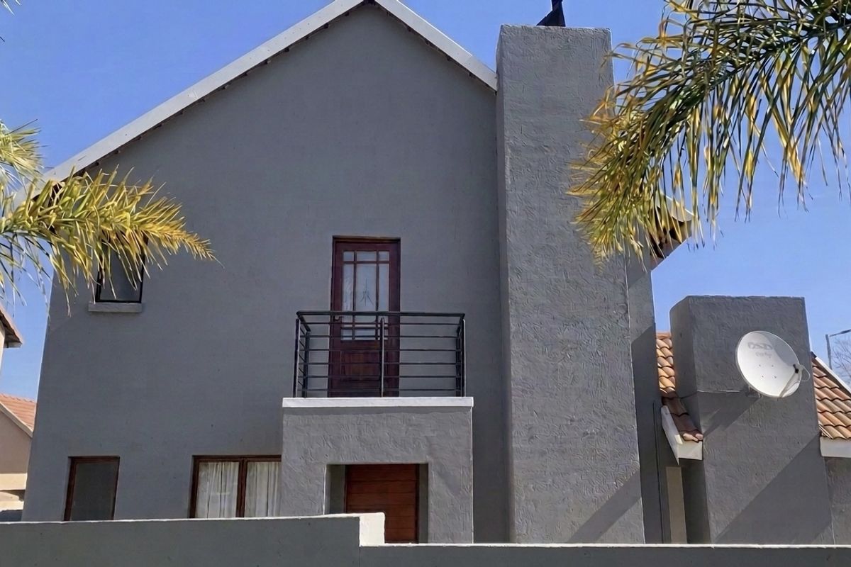 Rear elevation of a two-story house featuring a balcony with metal railing, a prominent chimney, and a tiled roof.