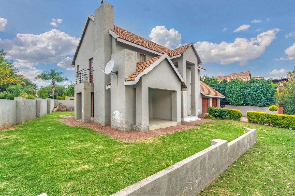 A view of the rear exterior of a multi-story house featuring a tiled roof, paved patio area, and surrounding lawn with boundary walls.