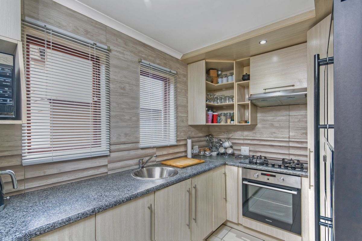 A compact, well-maintained kitchen featuring light wood-grain cabinetry, granite countertops, a built-in oven, gas hob, and stainless steel sink.