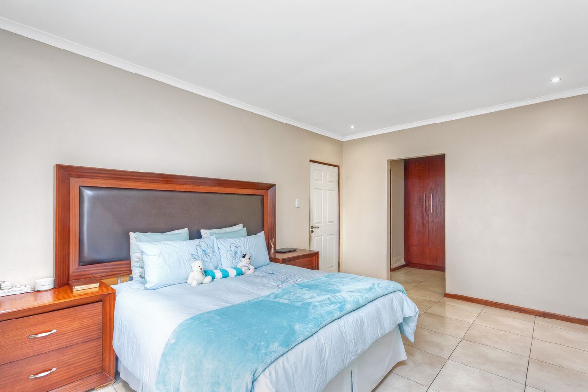 A spacious bedroom featuring neutral wall tones, tiled flooring, recessed ceiling lighting, and built-in wooden cabinetry in the adjacent dressing area.