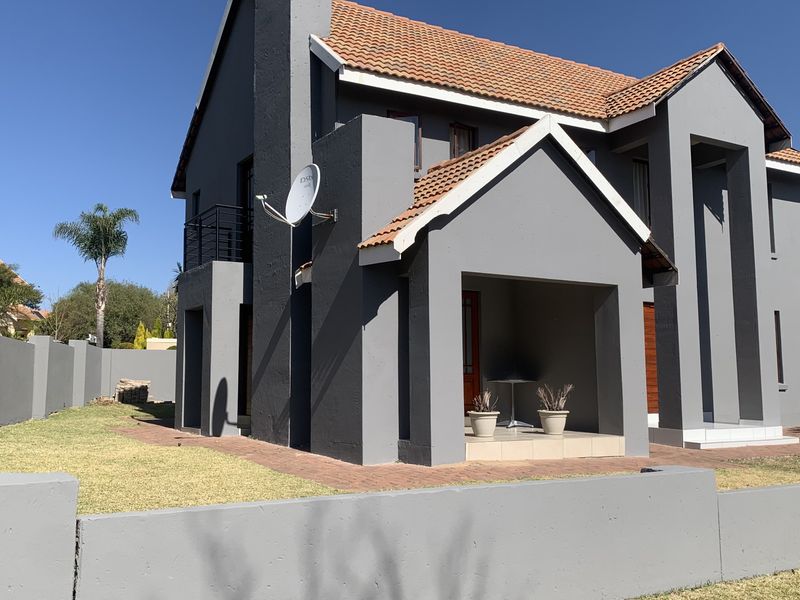 A modern double-story residential home featuring a grey facade, terracotta roof tiles, and a covered entrance porch with a surrounding boundary wall.