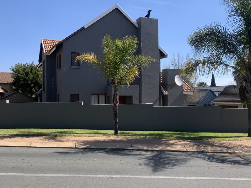 A view of the front elevation of a modern two-story house featuring a grey exterior, terracotta roof tiles, and a secure perimeter wall.