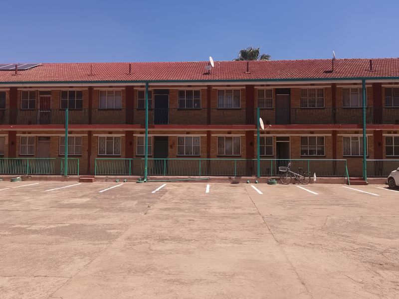 Front elevation of a multi-story brick apartment complex featuring a tiled roof, balcony access, and a paved parking area.
