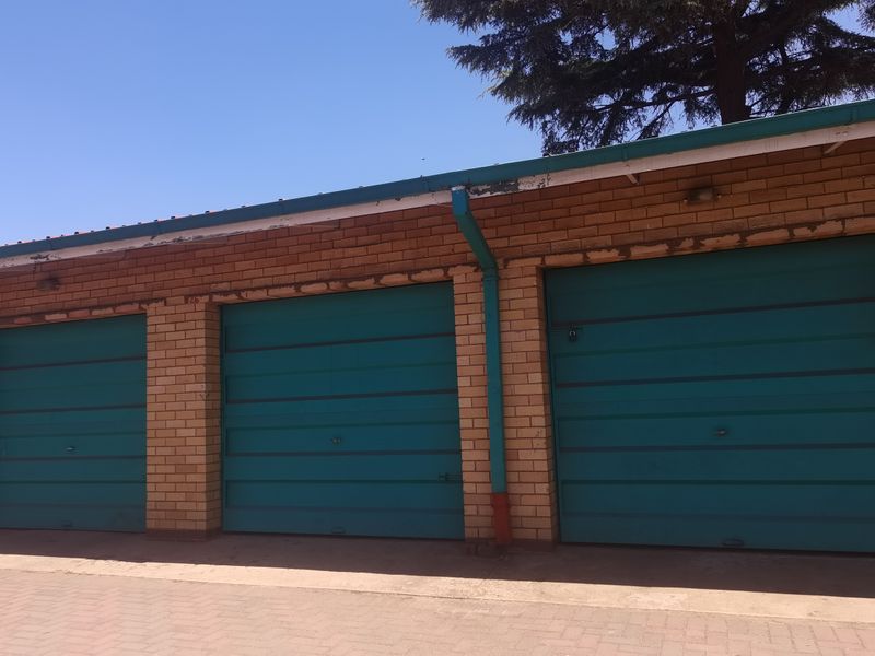 A row of three garage units featuring brick construction and teal-colored doors, situated on a paved driveway area.