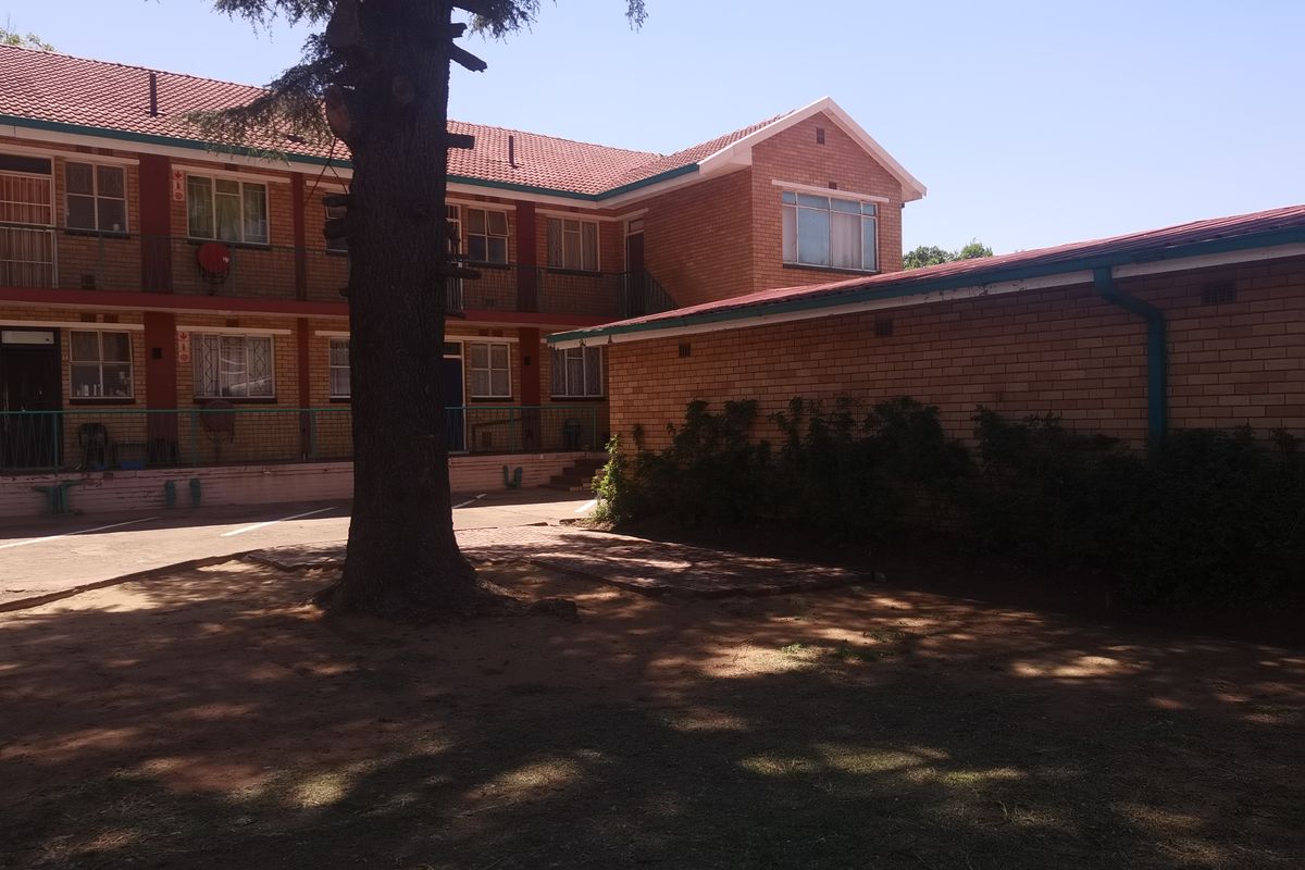 Exterior view of a multi-story face brick apartment complex featuring a paved courtyard area and mature landscaping.