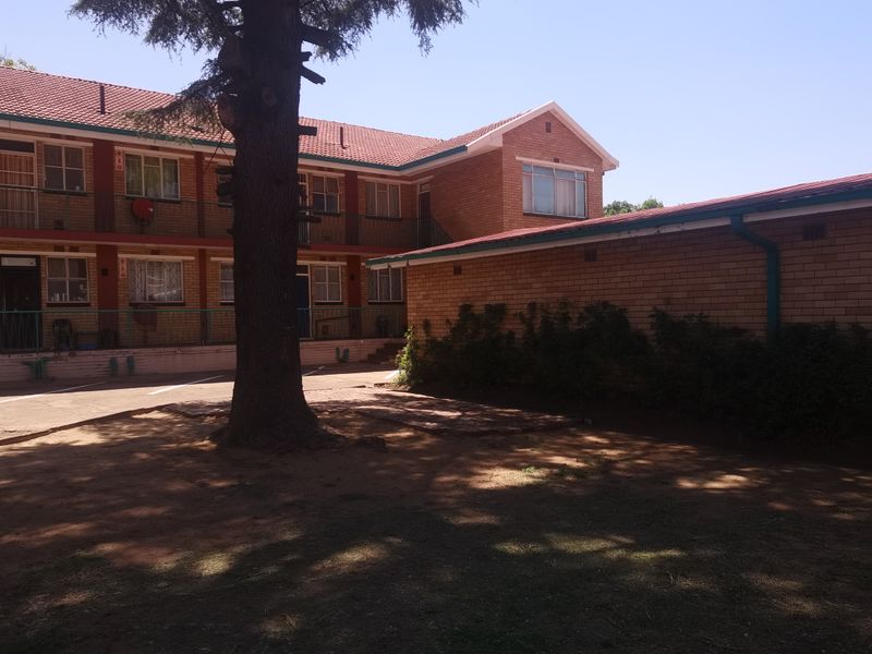 Exterior view of a multi-story face brick apartment complex featuring a paved courtyard area and mature landscaping.