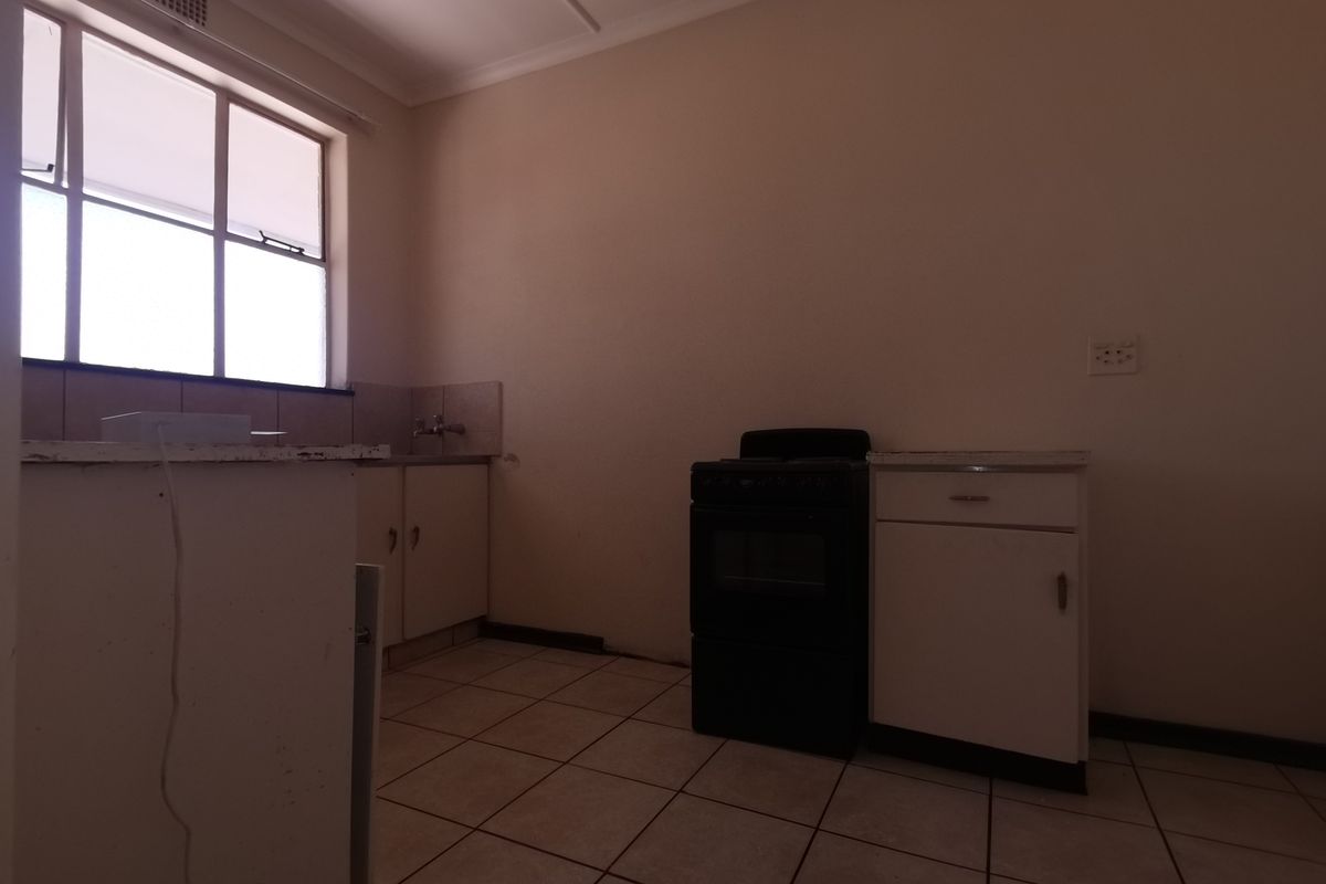 A basic, empty kitchen featuring tiled flooring, built-in cabinetry, a sink, and a freestanding stove, offering a blank canvas for renovation.