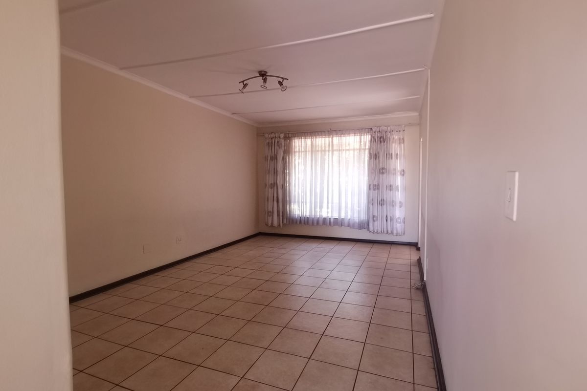 A spacious, empty living room featuring neutral tiled flooring, clean walls, and a ceiling-mounted track light fixture, ready for personalization.