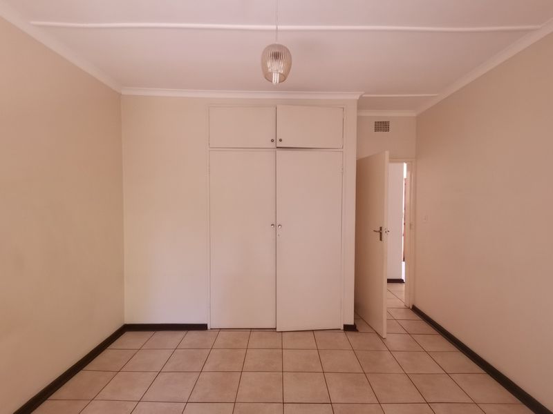 An empty bedroom featuring neutral walls, tiled flooring, and built-in storage cupboards.